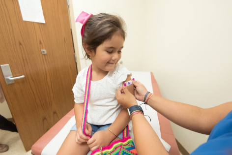 A little girl gets a sticker on her arm. 